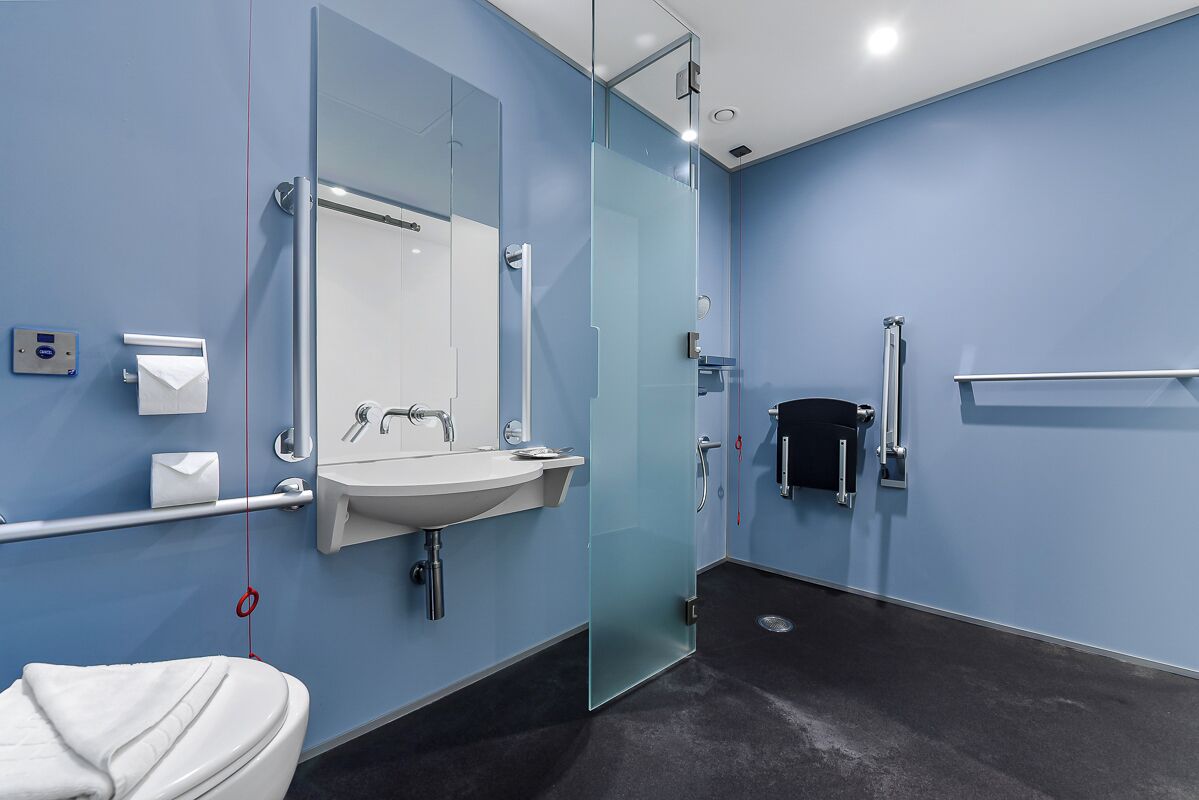 A modern bathroom with a glass shower enclosure, a white sink, and a hand dryer.