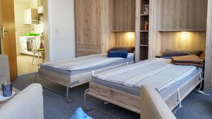 Habitación pequeña con dos camas individuales, un armario de madera y una kitchenette.