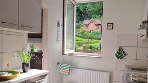 Una cocina moderna con armarios blancos, una ventana con vista a un jardín, un radiador y un cubo de basura.