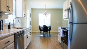 A modern kitchen with white cabinets, stainless steel appliances, and a dining area with a table and chairs. - Stylish and NEW! Duke~Art Deco (Durham)