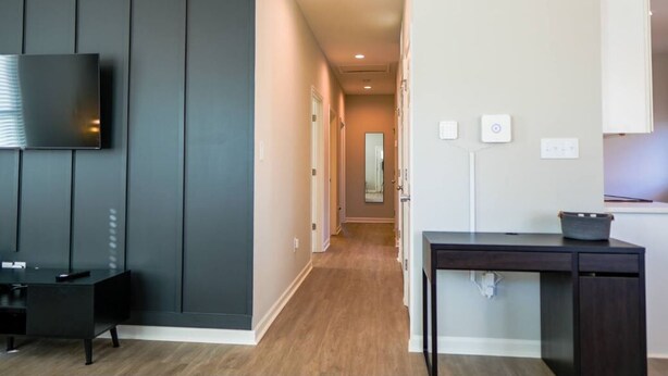 A modern hotel room with a flat-screen TV mounted on the wall, a dark wooden desk, and a small table with a basket. - Stylish and NEW! Duke~Art Deco (Durham)