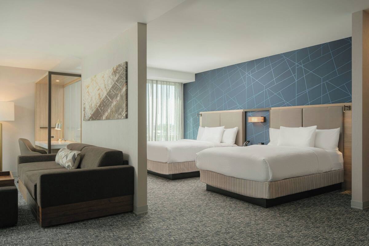A hotel room with two beds, a sofa, a desk, and a large window.