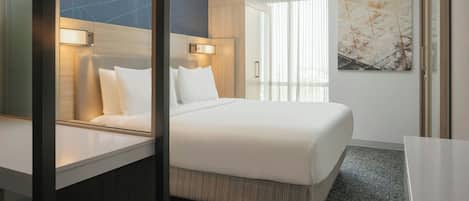 Una habitación de hotel moderna con una cama grande, una mesita de noche, un escritorio y un ventanal con cortinas.