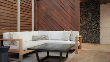 Uma área externa moderna com um sofá modular branco, uma mesa de centro escura e uma parede estampada.
