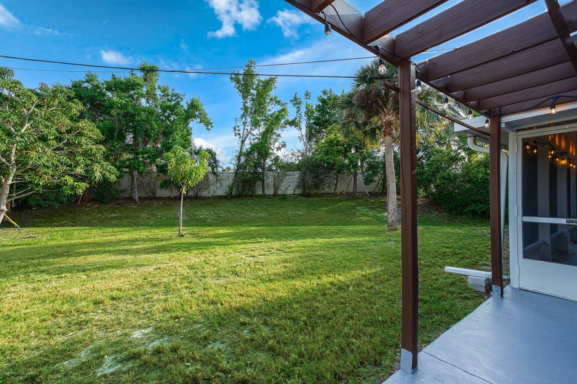 Un jardin avec une pergola en bois, une pelouse verdoyante et des arbres.