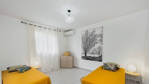 A bedroom with two beds, a nightstand, a wall-mounted air conditioner, and a large framed picture. - La Villa Armony (Lamentin)