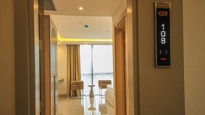A hotel hallway with a digital elevator display, a glass door, and a view of a balcony with a table and chairs. - GÖRGÜLÜ HOTEL (Kesan)