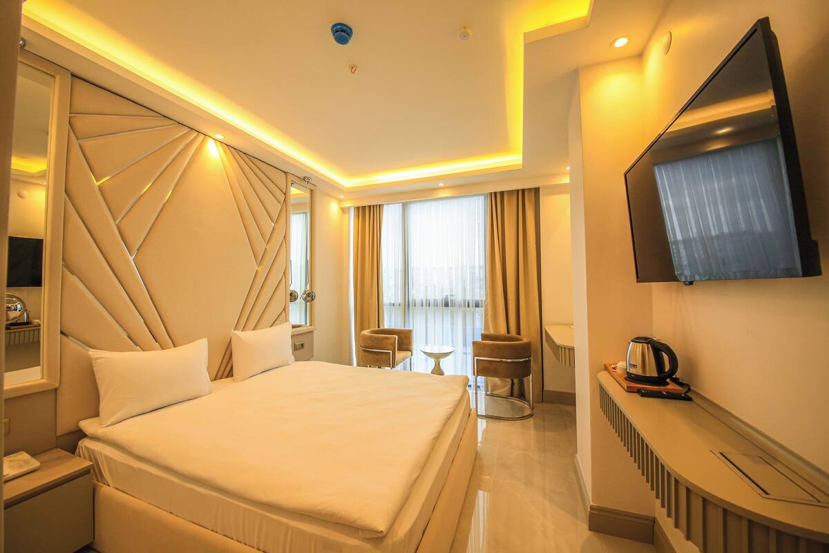 A hotel room with a large bed, a TV mounted on the wall, a small table, and a chair.