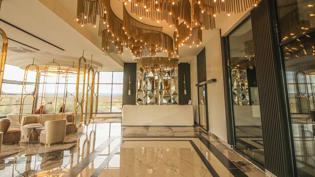 A spacious lobby with a high ceiling, a central reception desk, and a large glass wall offering a view of the outdoors. - GÖRGÜLÜ HOTEL (Kesan)