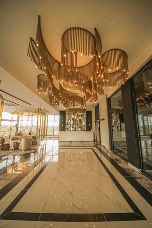 A spacious lobby with a high ceiling, a central reception desk, and a large glass wall offering a view of the outdoors. - GÖRGÜLÜ HOTEL (Kesan)