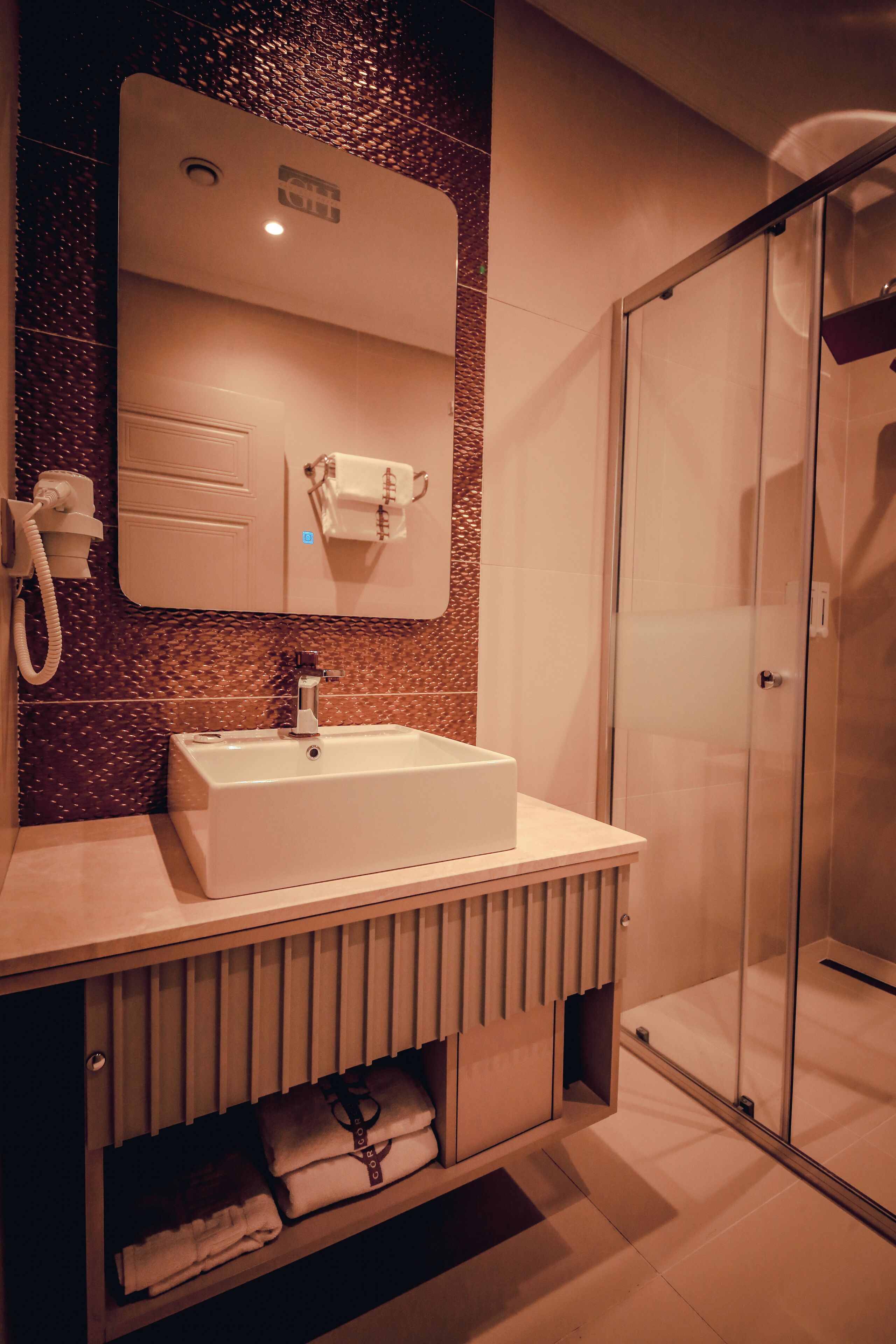 A modern bathroom with a white sink, a glass shower enclosure, and a marble backsplash.