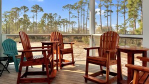 Une terrasse en bois avec des fauteuils Adirondack et une table, donnant sur une zone boisée.