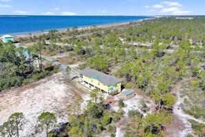 A single-story house with a porch, surrounded by a forested area and a beach in the background. - Dolphin Daze Beach House (Port St. Joe)