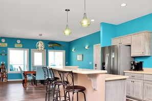 A kitchen with a turquoise wall, wooden bar stools, a stainless steel refrigerator, and a coffee maker. - Dolphin Daze Beach House (Port St. Joe)