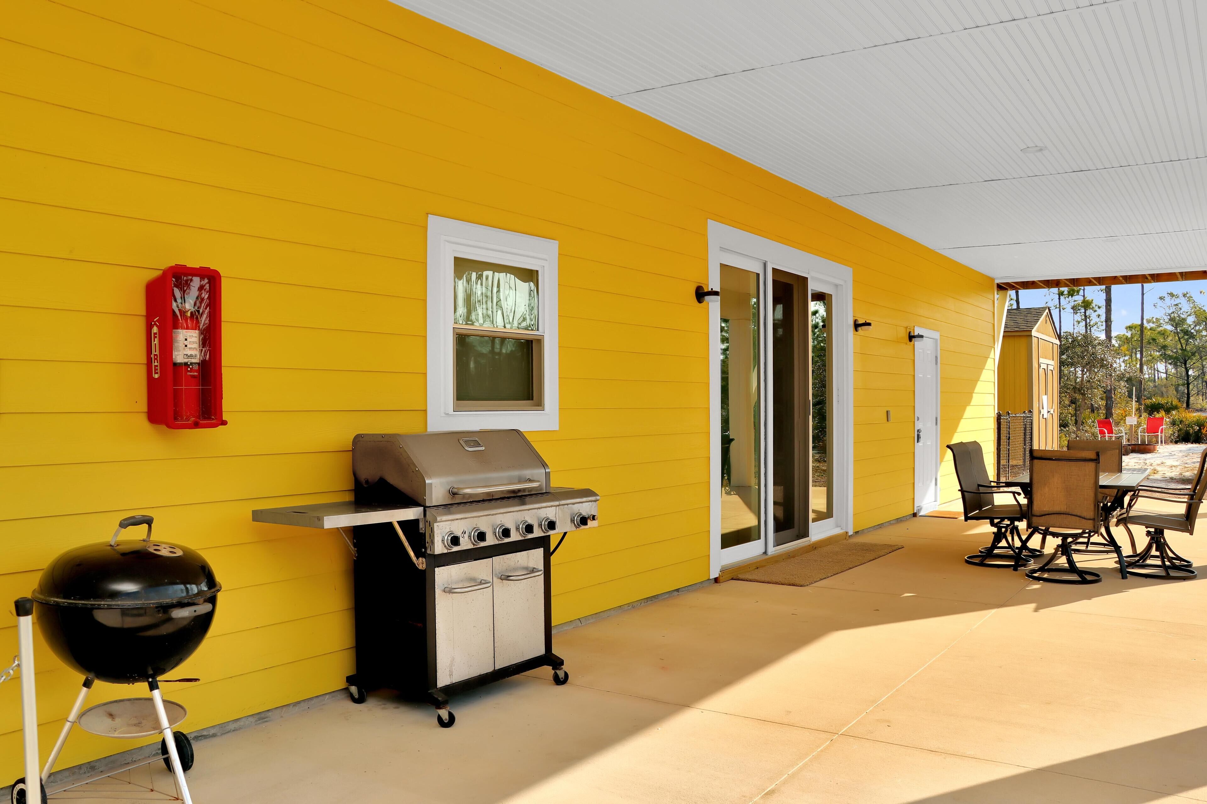 A yellow building with a covered patio, a barbecue grill, and outdoor seating.