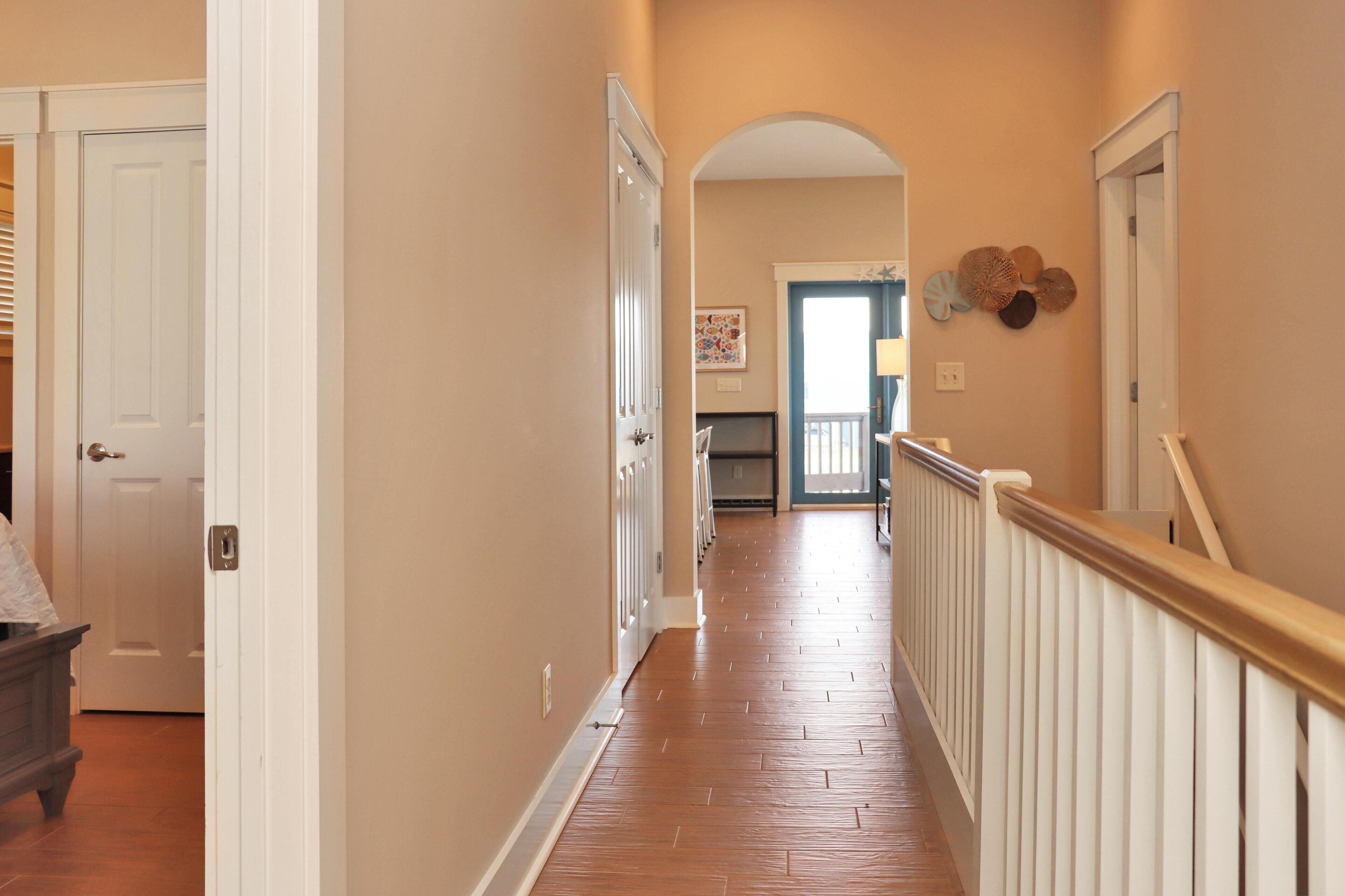 A hallway with a wooden floor, white railings, and a door on the left.