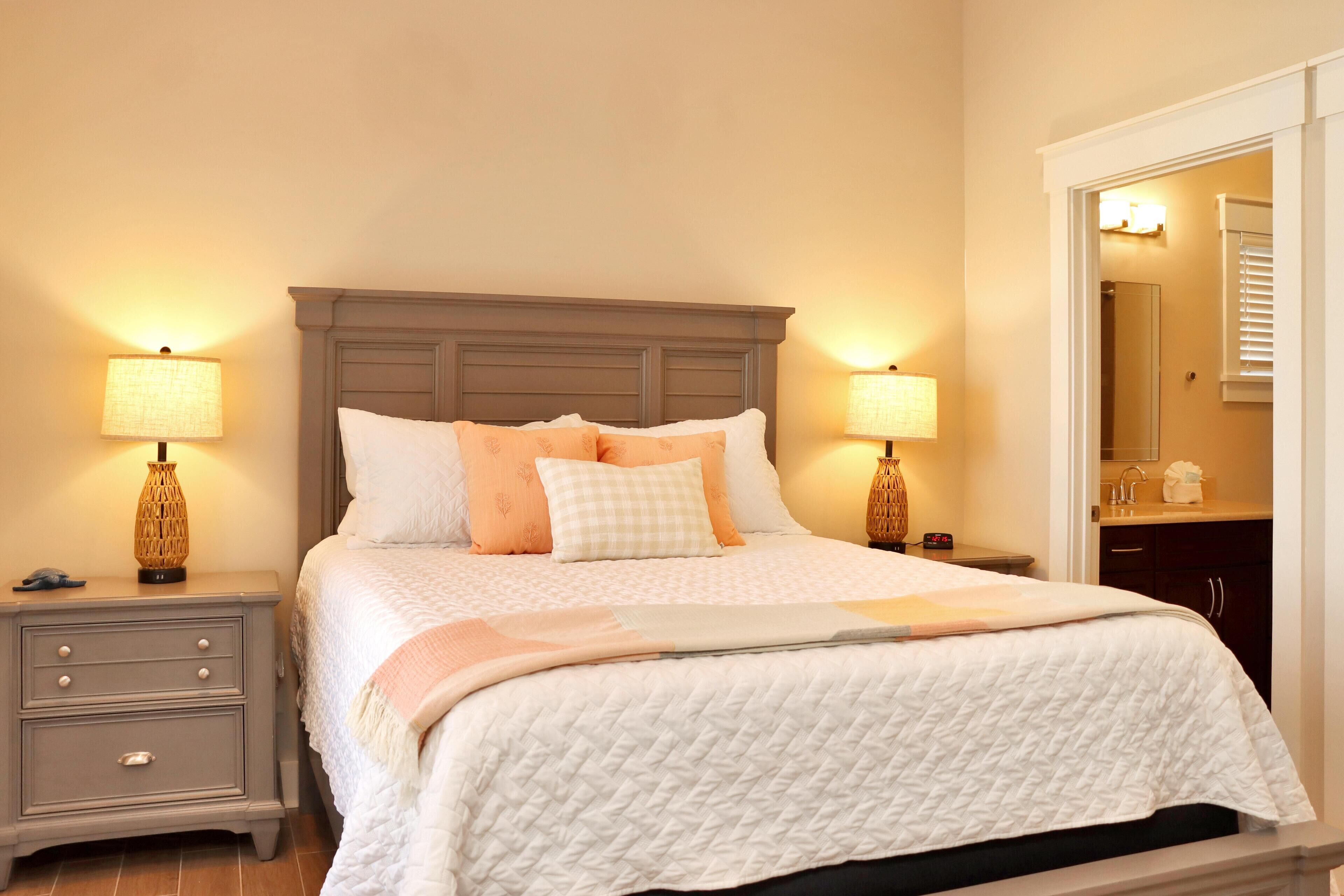 A neatly made bed with a quilted white duvet, two bedside tables with lamps, and a nightstand with drawers.