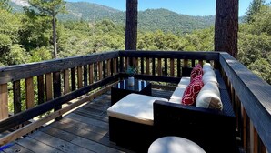 Une terrasse en bois avec des sièges d’extérieur, une table ronde et une vue sur une colline boisée.