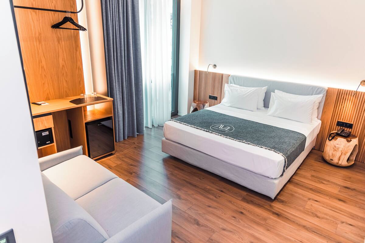 A modern hotel room with a large bed, a desk, and a wardrobe.