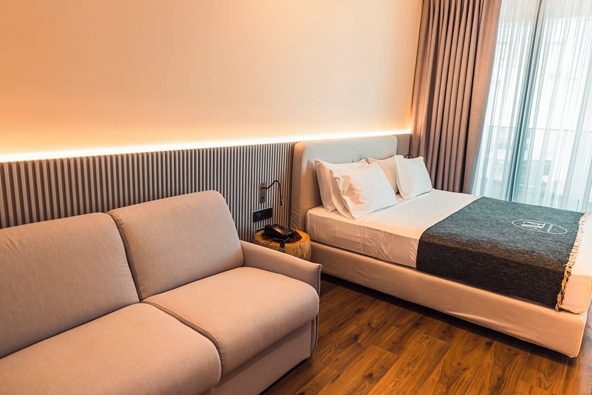 A hotel room with a sofa, a bed, a nightstand, and a telephone.