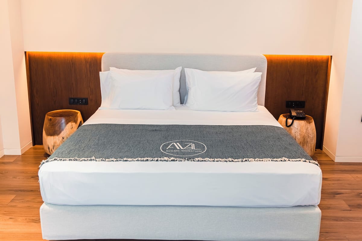 A bed with a grey blanket, white pillows, and a wooden headboard. There are two bedside tables with lamps and a phone on one.