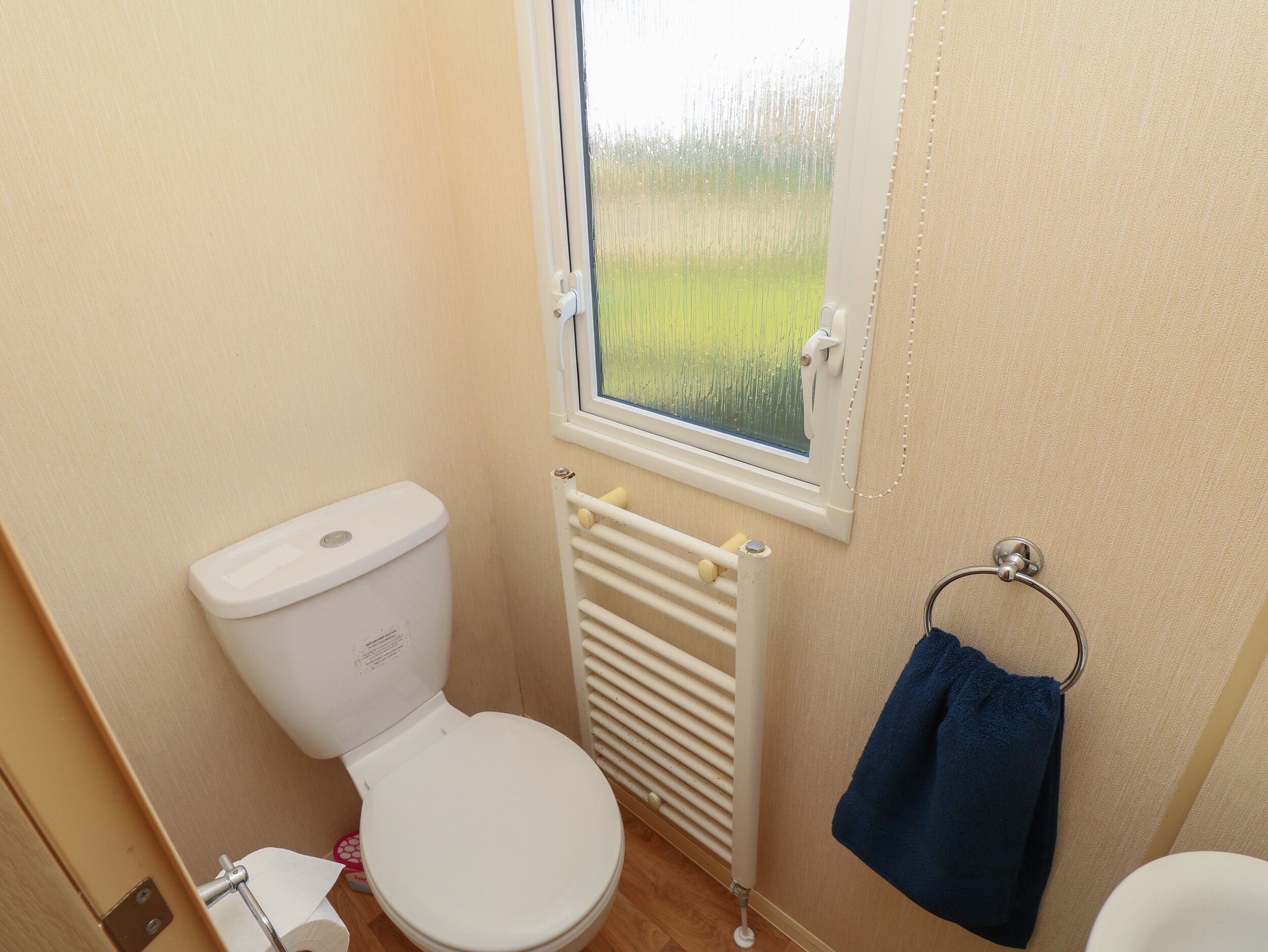 A compact bathroom with a toilet, a window, a radiator, and a towel rack.