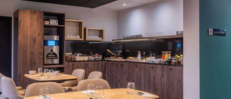 Un espace repas moderne avec des tables et des chaises en bois, ainsi qu’un comptoir de cuisine où sont disposés divers objets.