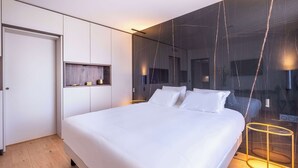 Une chambre à coucher moderne avec un grand lit, une table de chevet, un miroir et une étagère fixée au mur.