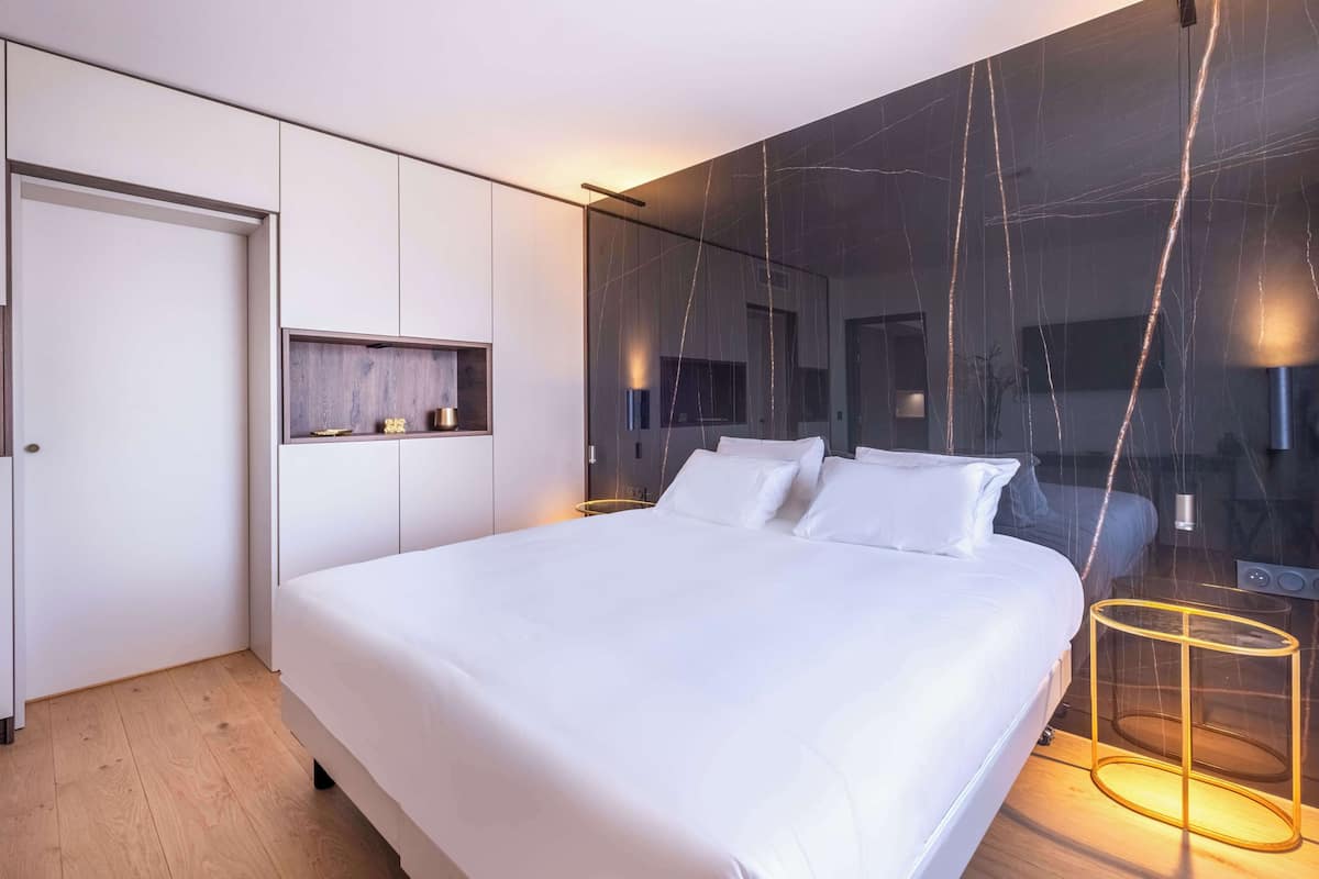 Een moderne slaapkamer met een groot bed, een nachtkastje, een spiegel en een wandplank.