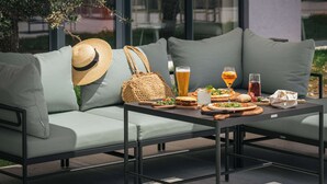 Un espace extérieur aménagé avec des sièges et une table dressée pour un repas, comprenant des pizzas, des boissons et un panier.