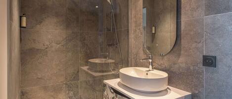 A modern bathroom with a large white sink, a handheld showerhead, and a wall-mounted mirror.