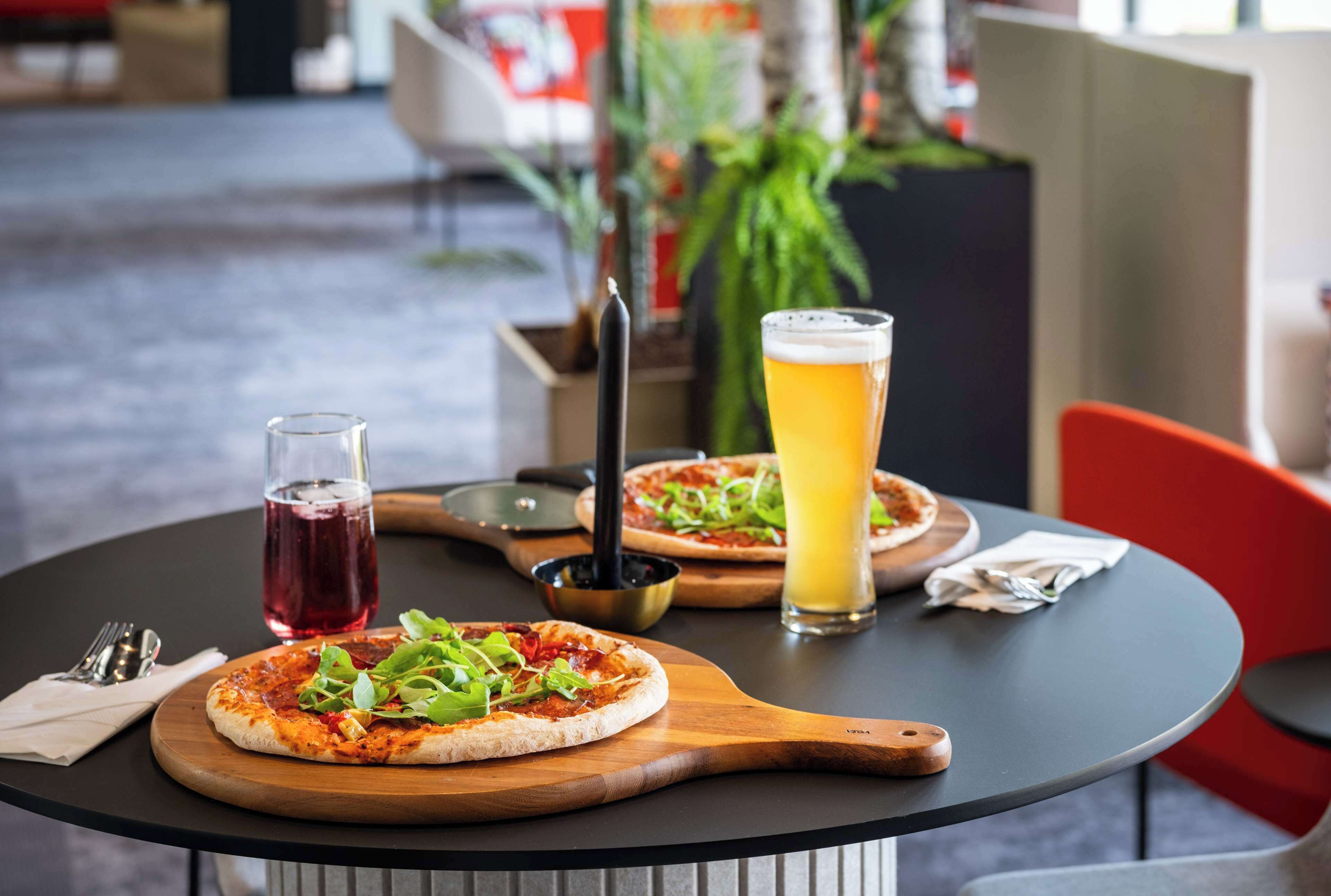Una mesa con dos pizzas sobre tablas de madera, una cerveza y un vaso de bebida roja.