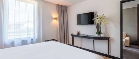 Habitación de hotel con una cama grande, un televisor de pantalla plana montado en la pared, una mesita de noche con un florero y un espejo grande.
