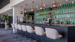 Un espace bar doté d’un long comptoir, de nombreux tabourets et d’un mur recouvert de carreaux verts, avec des étagères remplies de bouteilles.