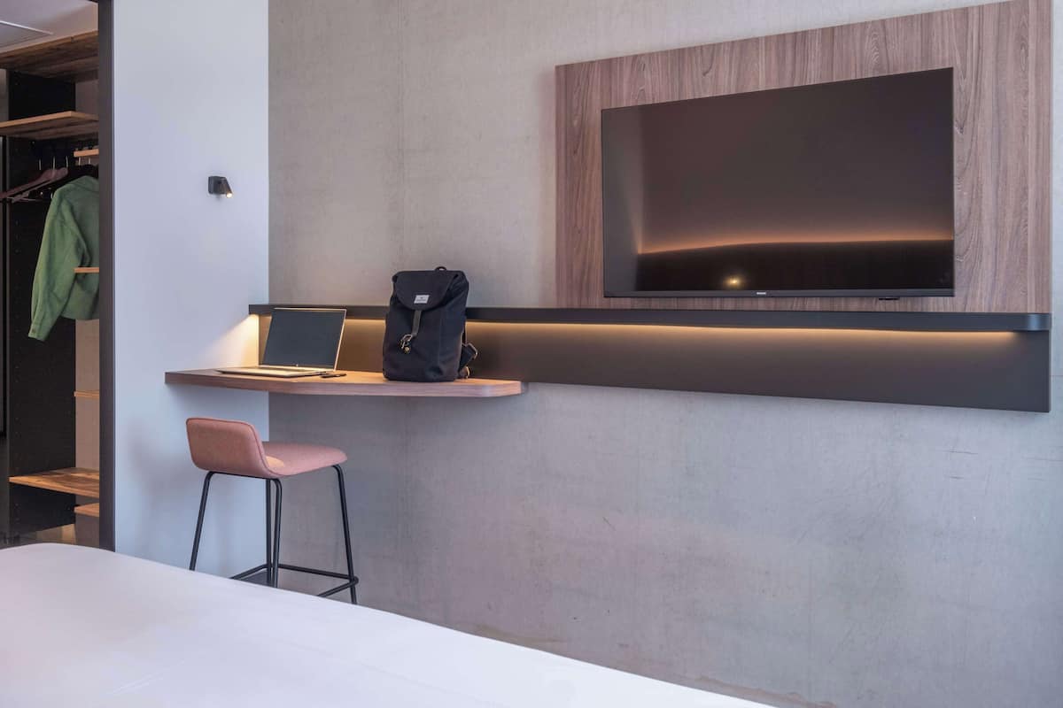 Een moderne kamer met een ingebouwd bureau, een laptop, een rugzak en een aan de muur bevestigde televisie.