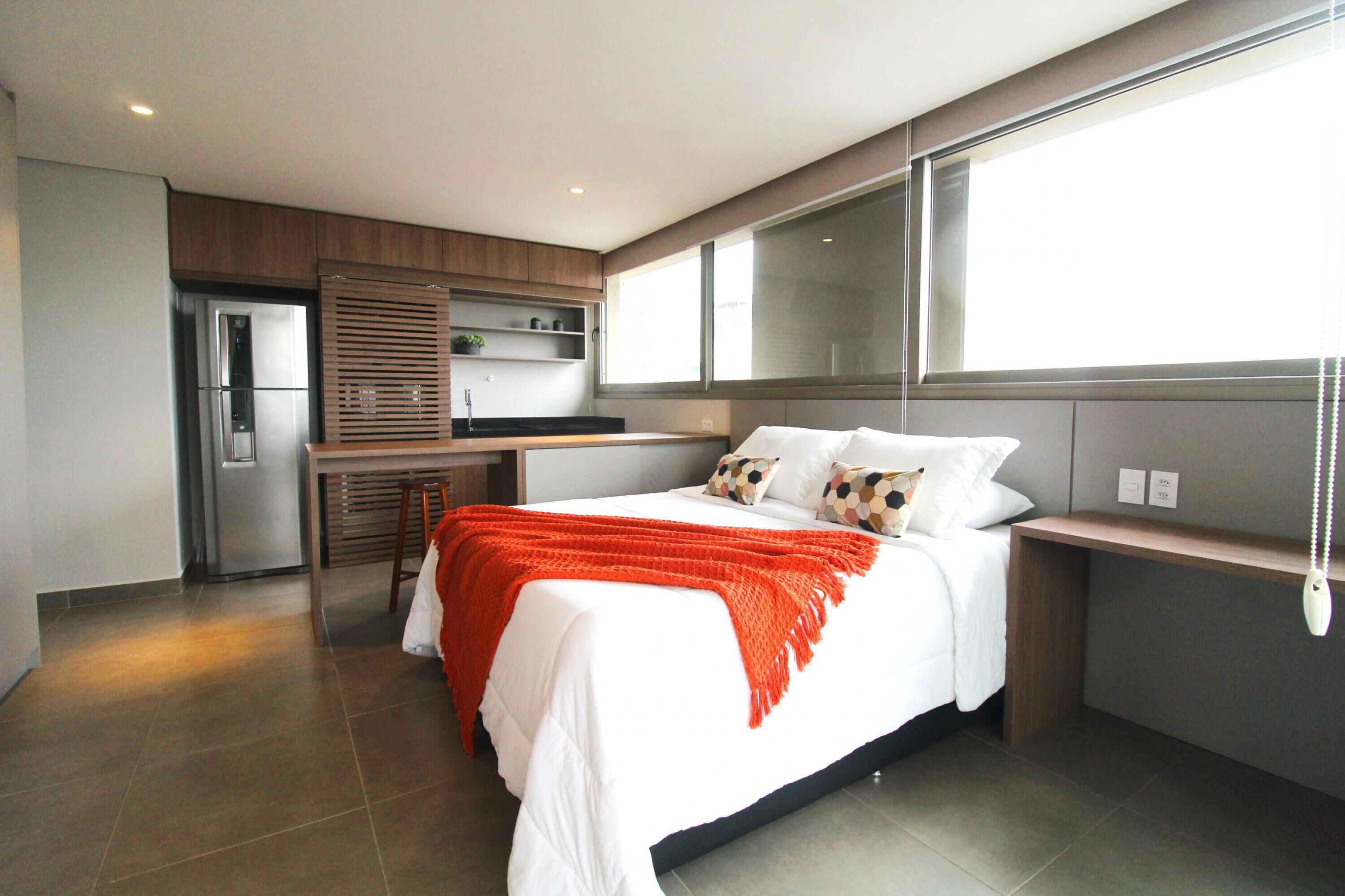 Un dormitorio moderno con una cama grande, un escritorio empotrado y una zona de cocina.