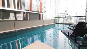 A swimming pool with lounge chairs and a high-rise building in the background. - Melo 1701 in S o Paulo (São Paulo)
