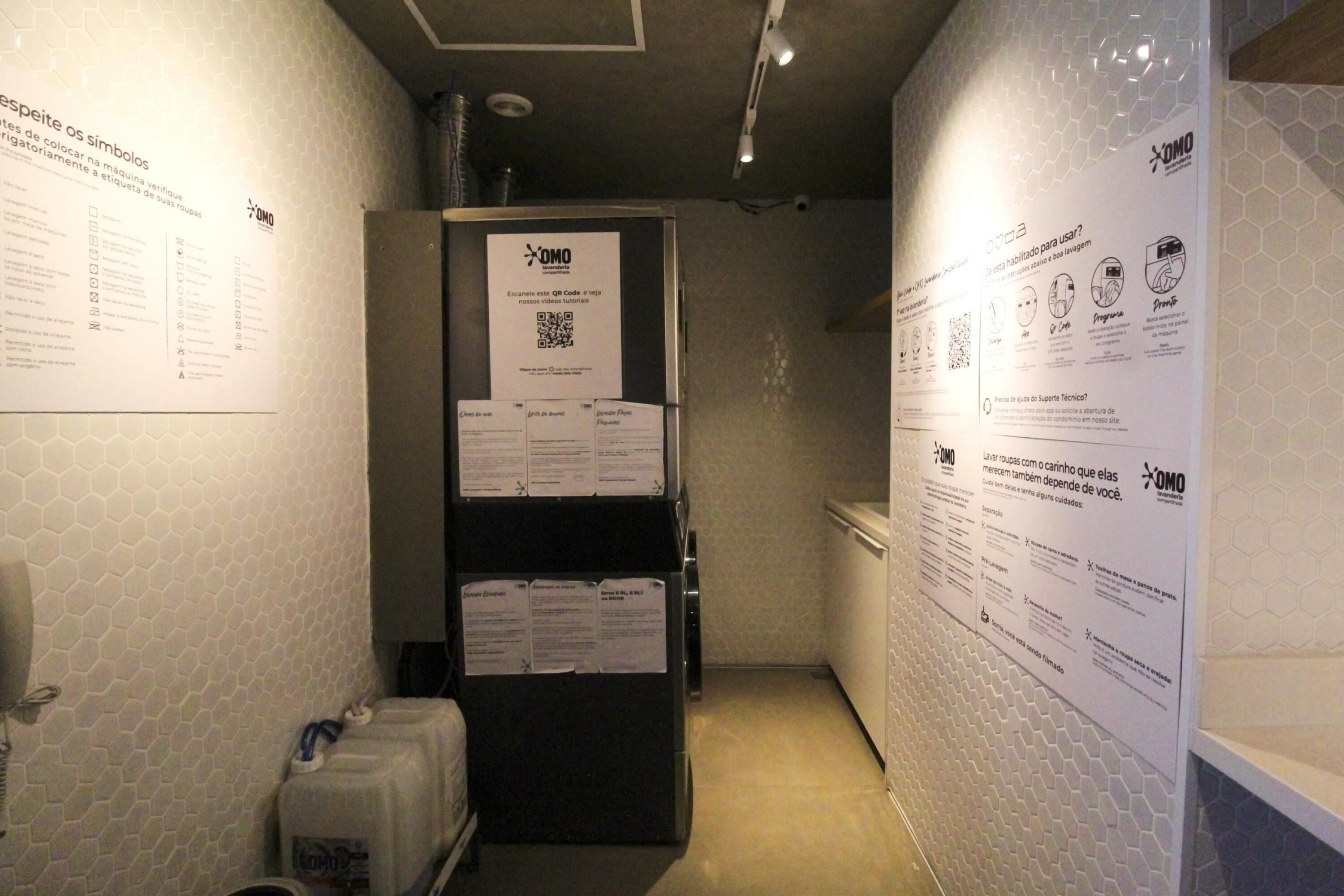 A narrow hallway with a refrigerator and a sink on one side, and a wall with informational posters on the other.