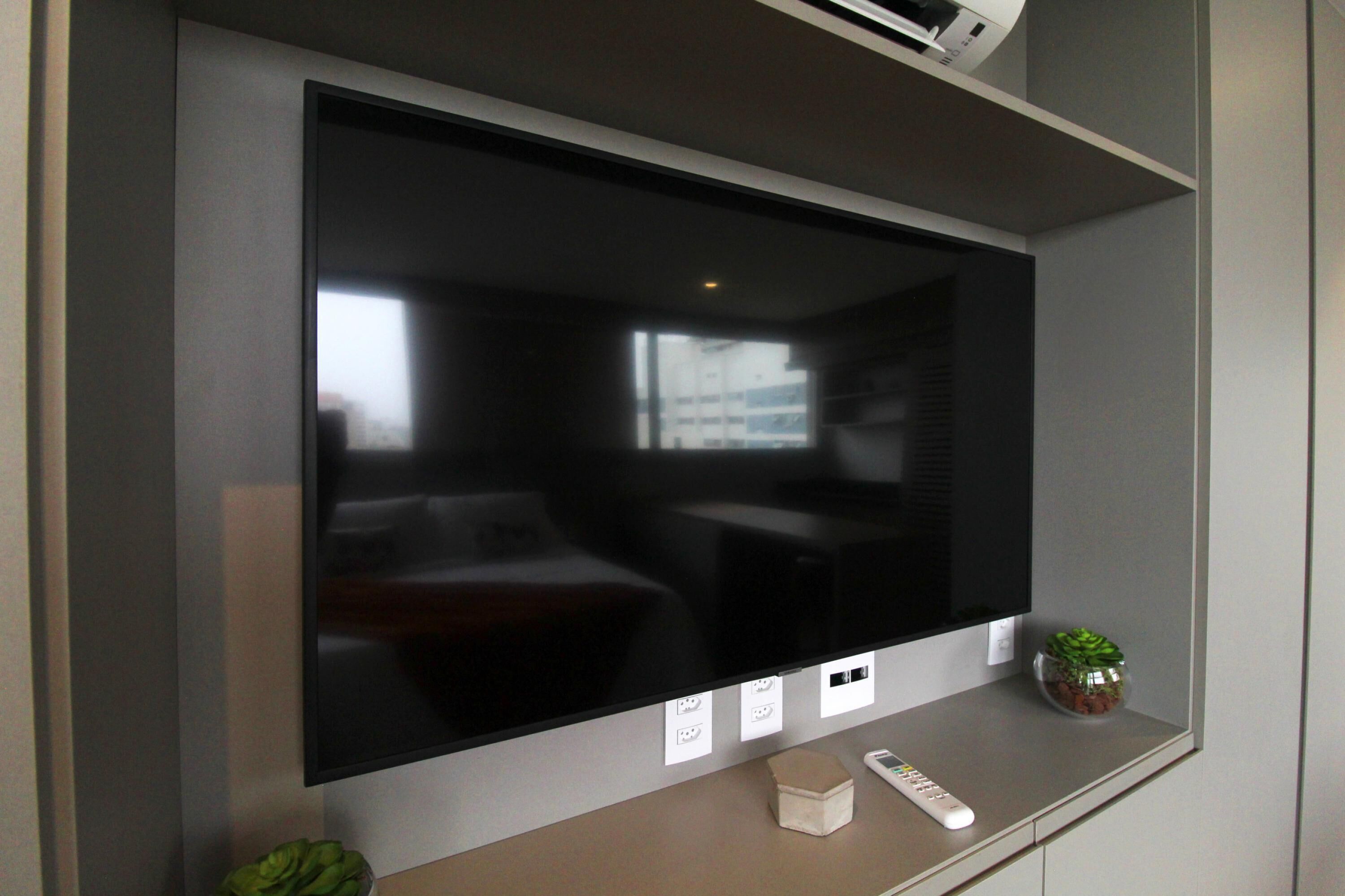 A modern living room with a large flat-screen TV mounted on the wall, a small potted plant, a remote control, and a power outlet.