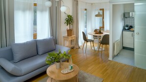 A modern living room with a sofa, a dining table with chairs, a small kitchen area, and a potted plant.