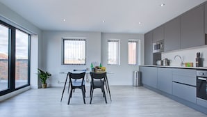 A modern kitchen with grey cabinets, a microwave, and a sink. There are two chairs and a table with a plant and a box on it. - Hybrid Resi - Uxbridge  (Uxbridge)