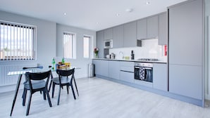 A modern kitchen with grey cabinets, a microwave, stove, and dishwasher. There is a dining table with chairs and a window with blinds. - Hybrid Resi - Uxbridge  (Uxbridge)