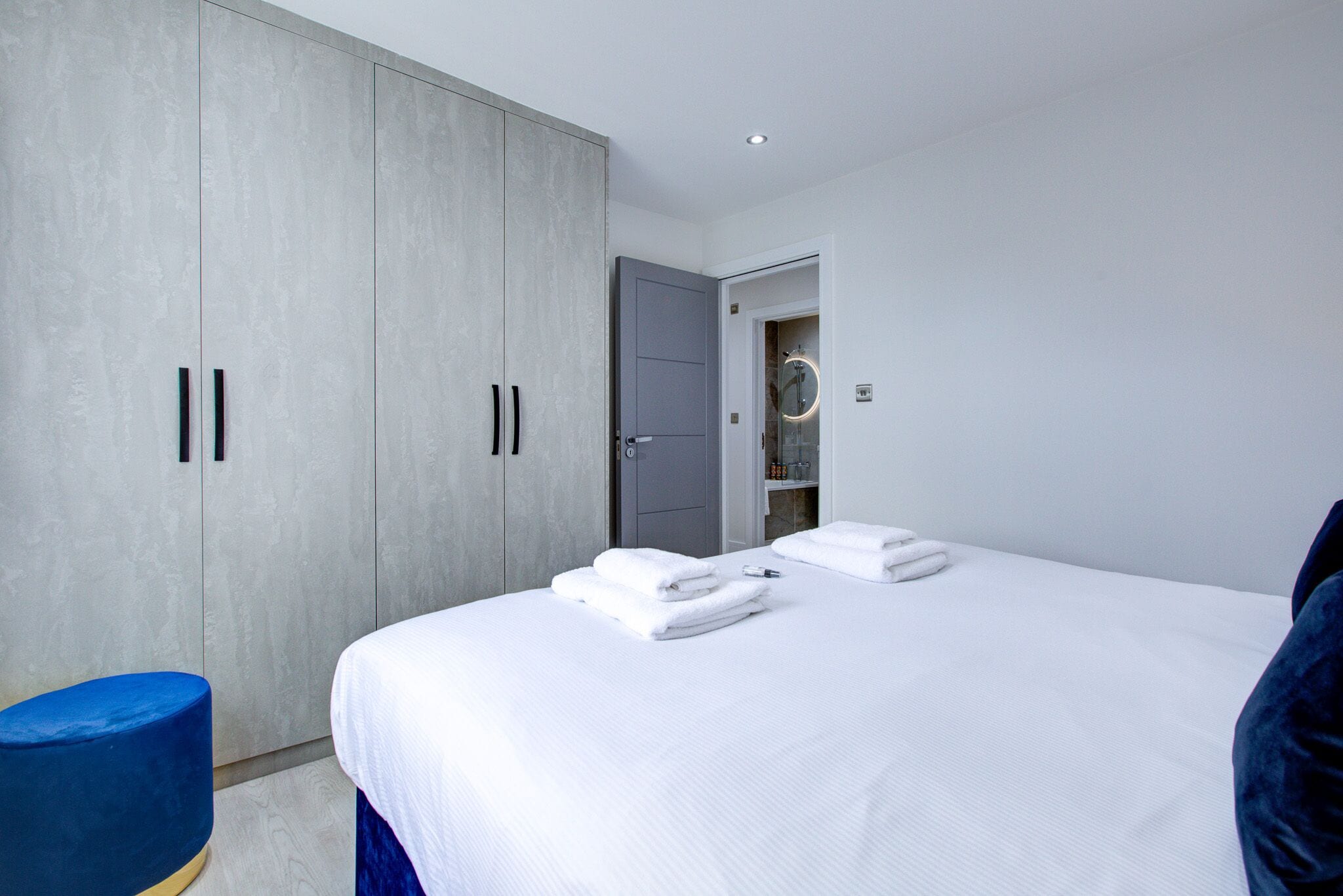 A modern bedroom with a large bed, a wardrobe, and a blue chair.