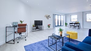 A modern living room with a sofa, coffee table, and a TV. There's a dining area with a table and chairs. - Hybrid Resi - Uxbridge  (Uxbridge)