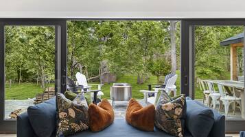 A modern living room with a large glass door leading to an outdoor patio, furnished with a sofa, chairs, and a grill.