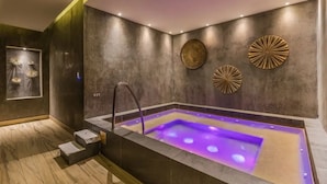 Ein moderner Wellnessraum mit warmer Fußbodenheizung, einer großen Badewanne mit violetter Beleuchtung und dekorativen Wandbildern.