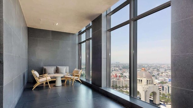 Une chambre moderne dotée d’une grande fenêtre, d’un coin salon avec une table et d’une vue sur le paysage urbain.