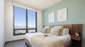 Une chambre avec une grande fenêtre, un lit doté d’une tête de lit en bois et deux tableaux encadrés accrochés au mur.