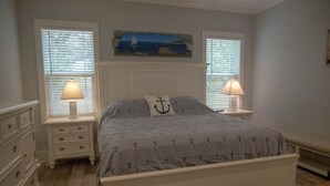 A bedroom with a bed, two bedside tables with lamps, a dresser, and a painting above the bed.