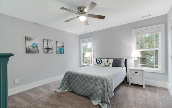 A bedroom with a bed, a nightstand, a ceiling fan, and a window.